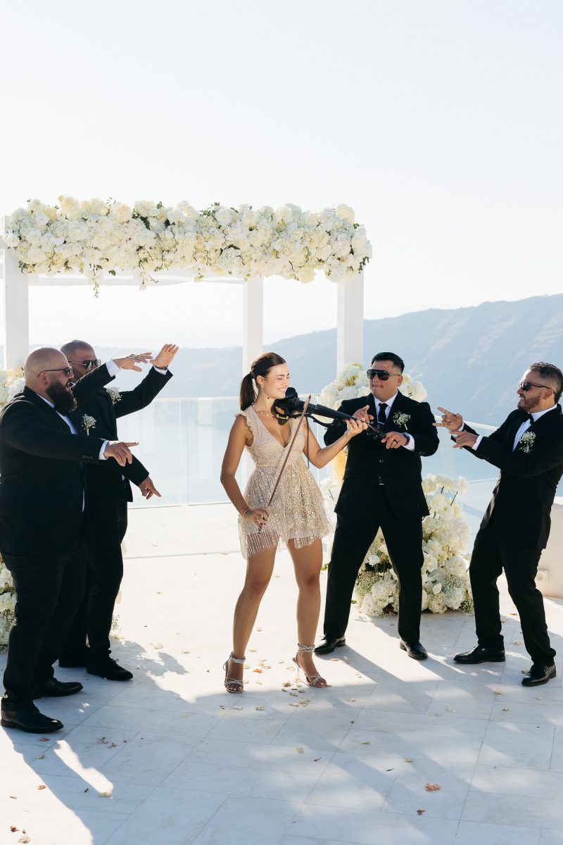 Groom and groomsmen celebrating with electric violinist at Santorini wedding by Santorini wedding photographer