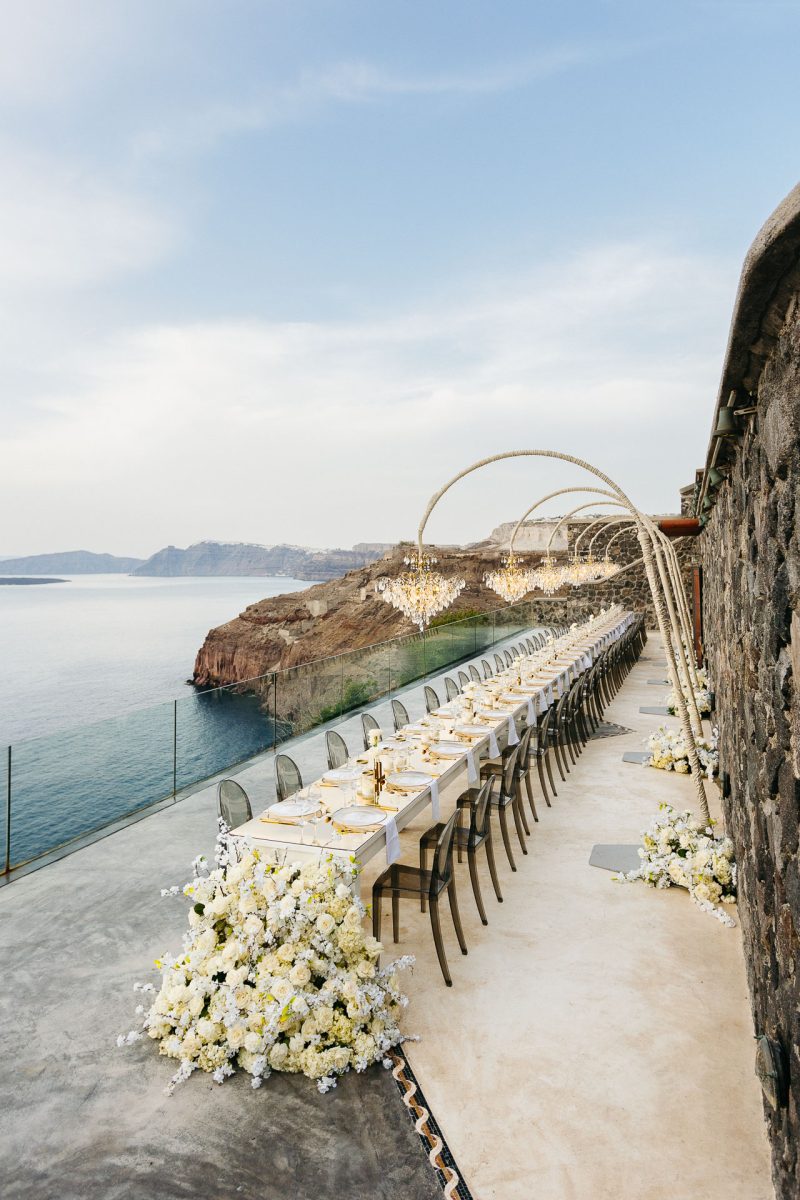 Santorini wedding photographer captures elegant cliffside reception table overlooking the caldera.