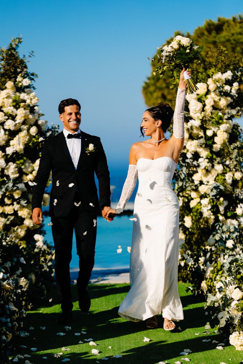 Santorini wedding photographer captures joyful newlyweds walking through floral aisle