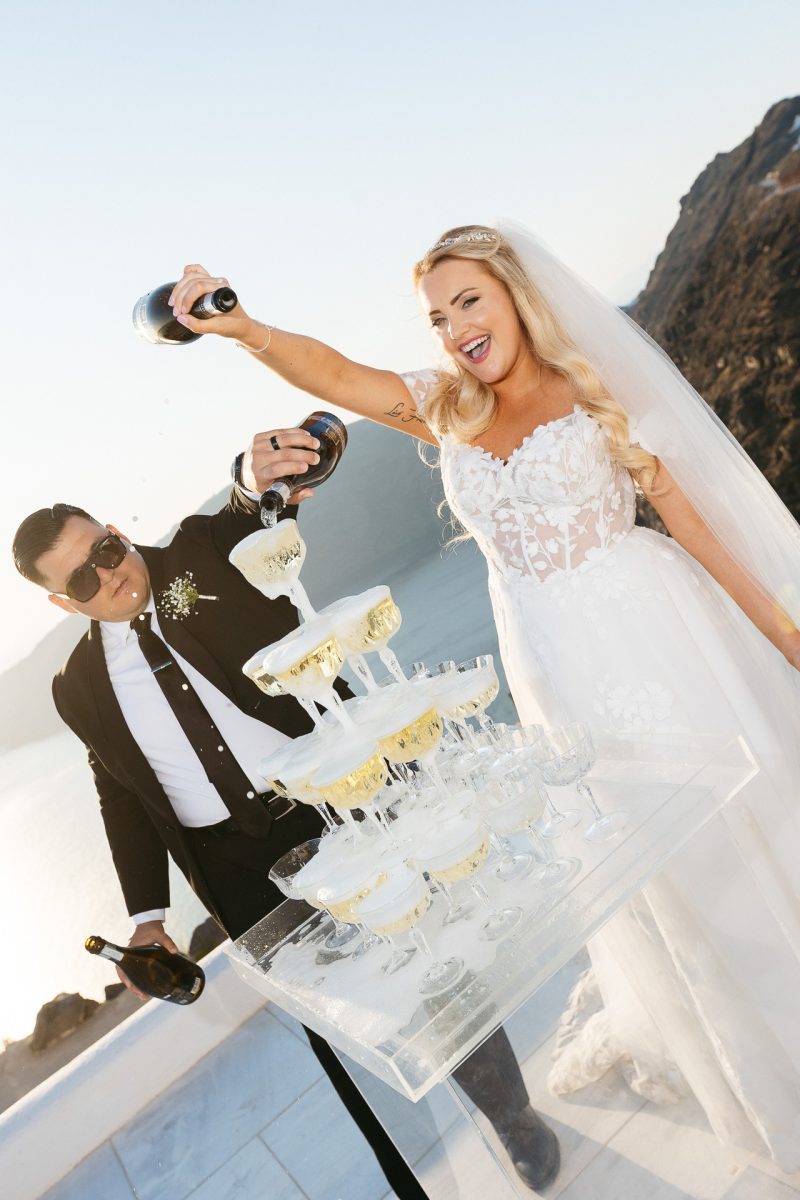 Bride and groom pouring champagne tower in Santorini by Santorini wedding photographer