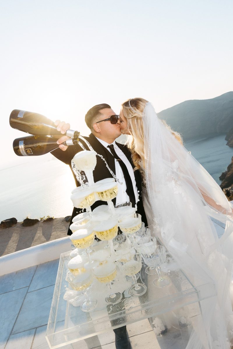 Bride and groom pouring champagne tower in Santorini by Santorini wedding photographer