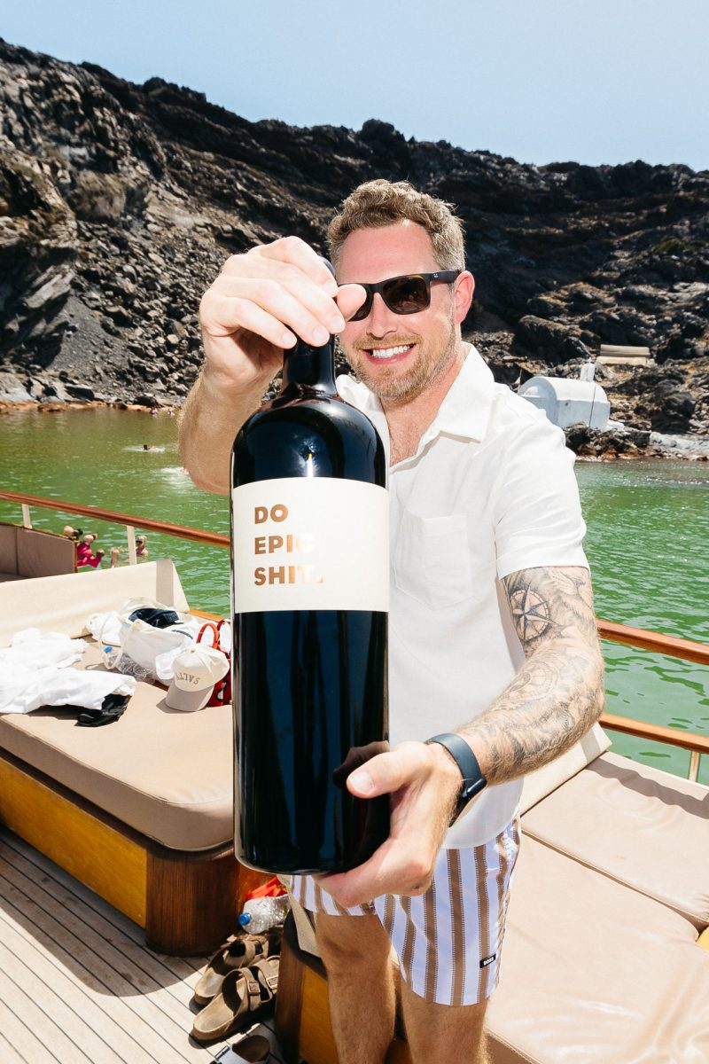 Santorini wedding photographer captures groom’s bold wine toast on boat.
