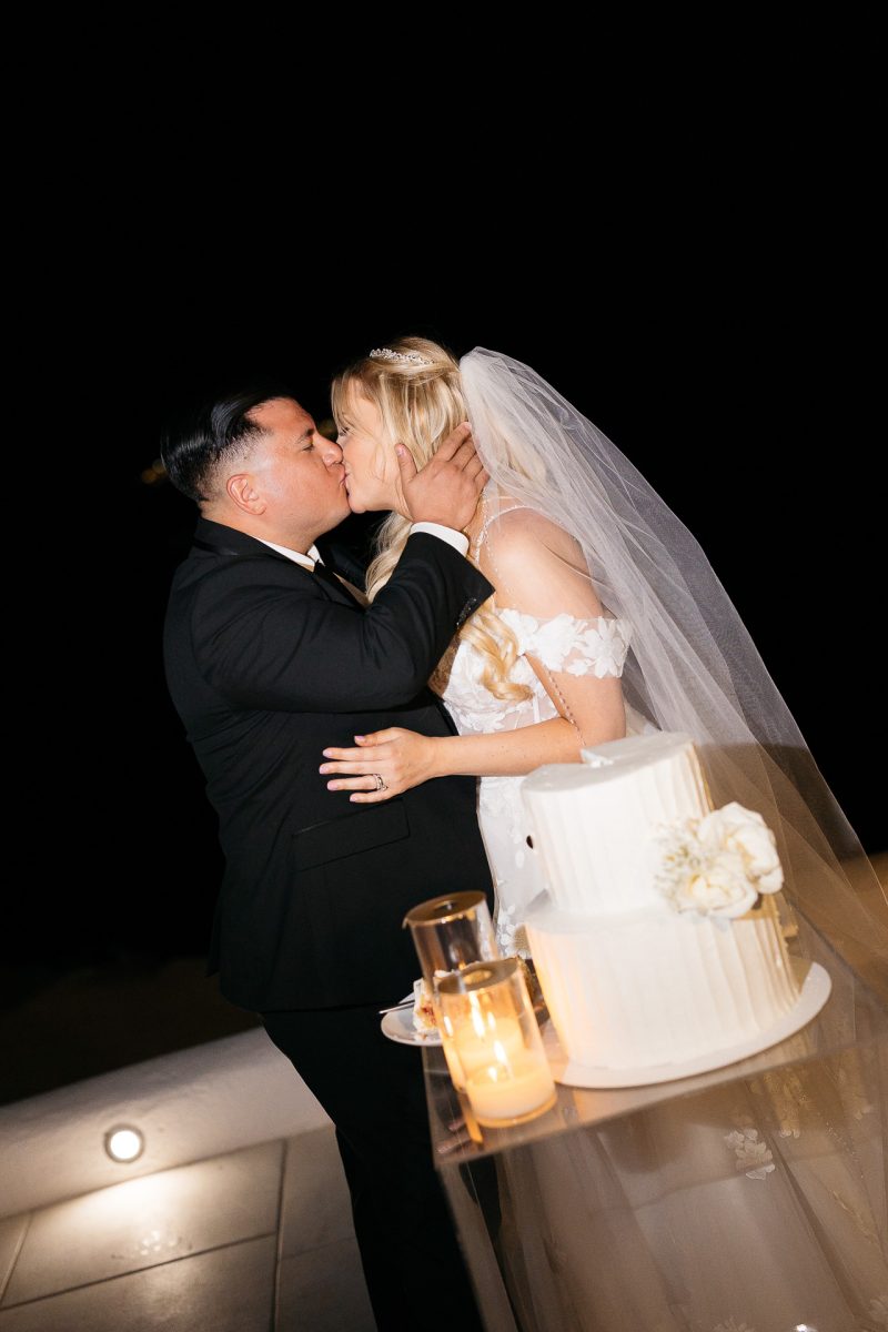 Bride and groom kissing after cake cutting by Santorini wedding photographer
