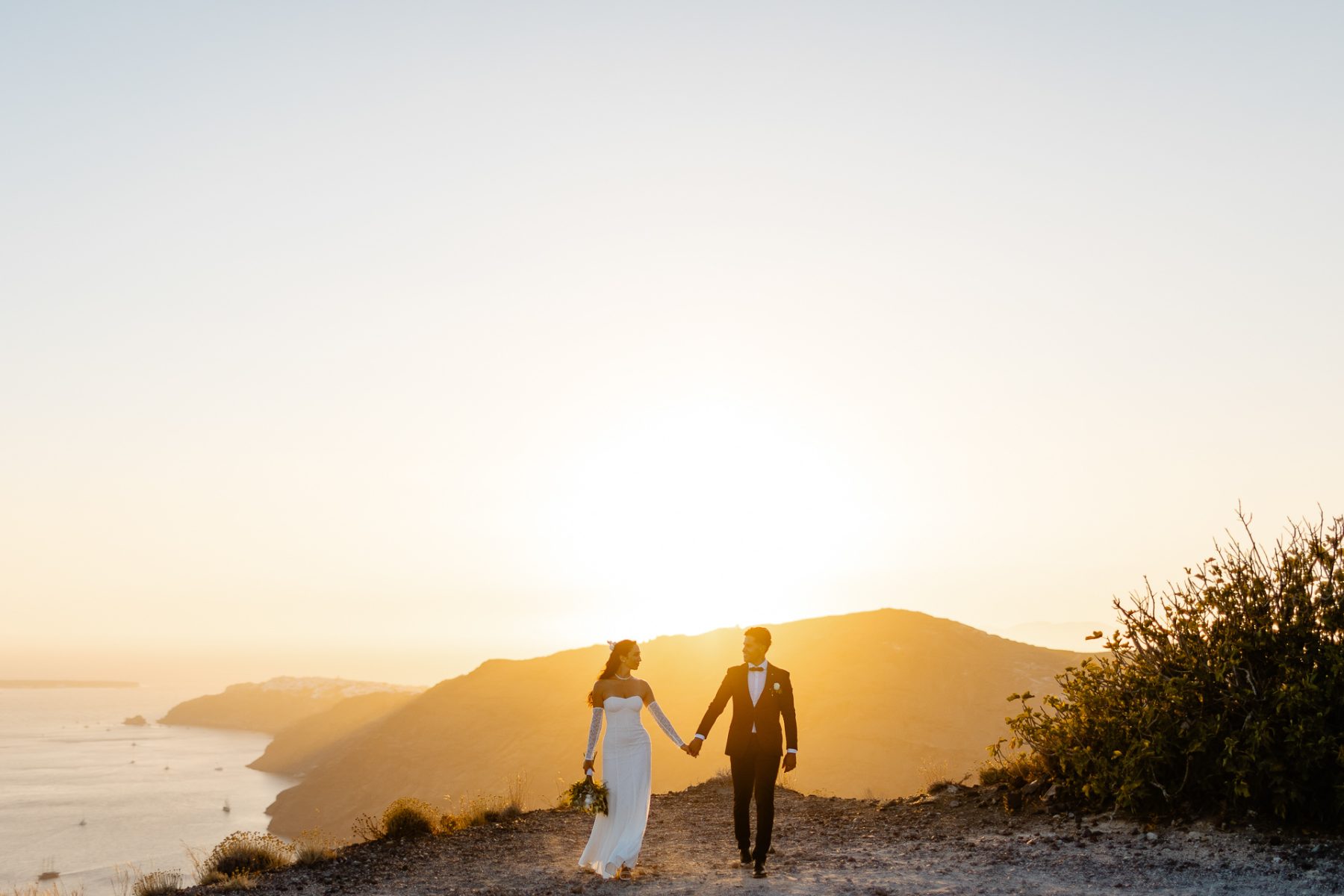 Santorini wedding photographer captures bride and groom walking at sunset