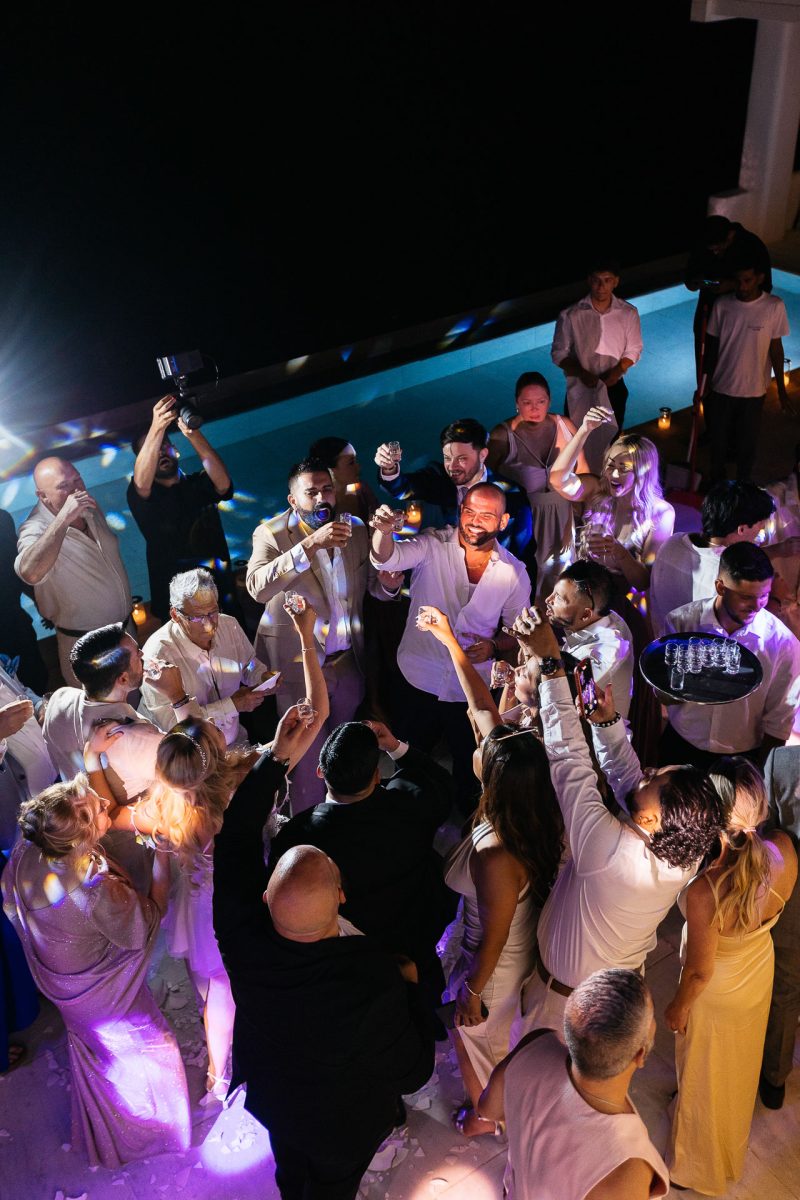 Wedding guests raising a toast at Santorini reception by Santorini wedding photographer