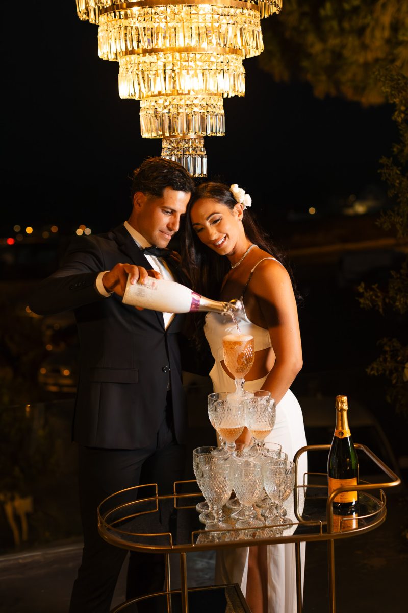 Santorini wedding photographer captures bride and groom pouring champagne tower