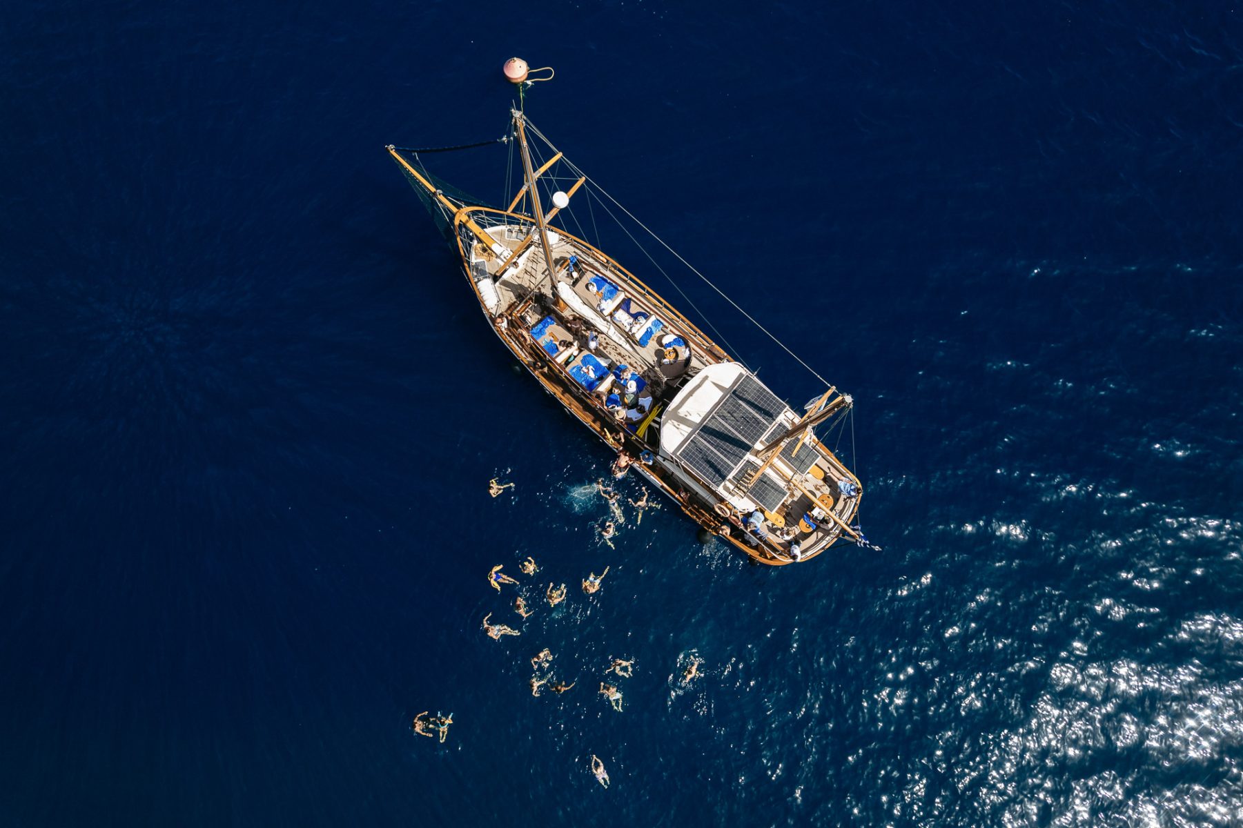 aerial view of a boat in Santorini with people swimming captured by Santorini wedding photographer