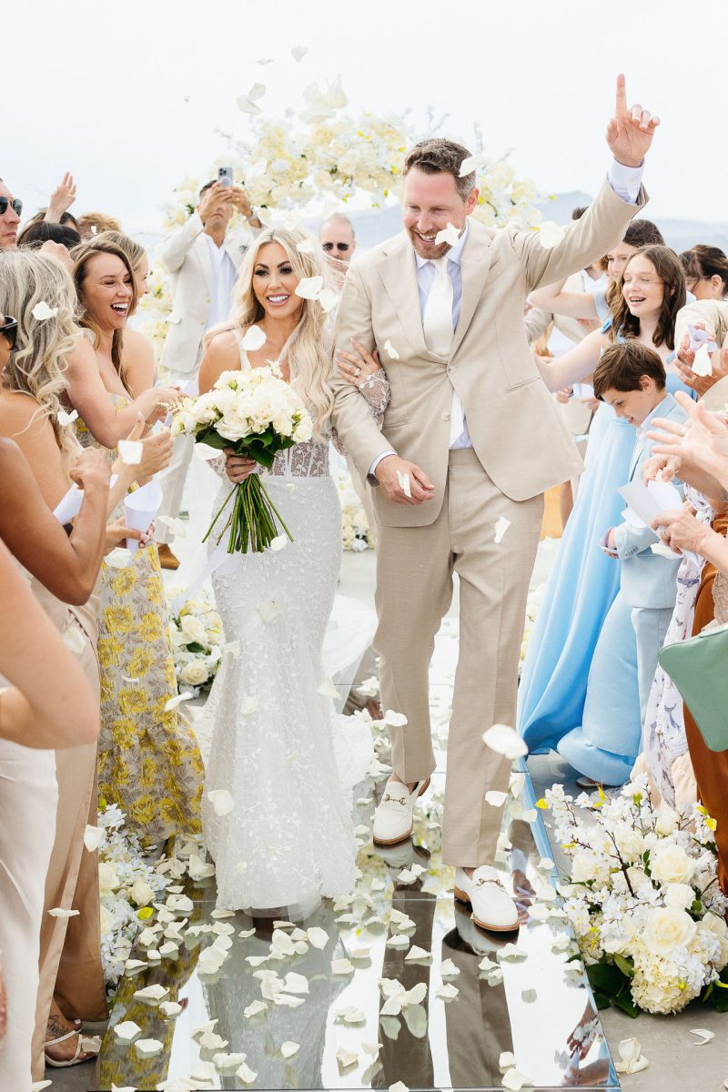 Bride and groom celebrated by guests with petals captured by Santorini wedding photographer.