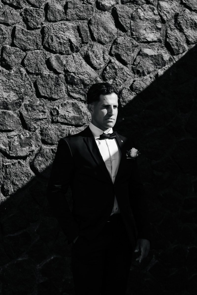 Groom in tuxedo standing in dramatic light, Santorini wedding photographer