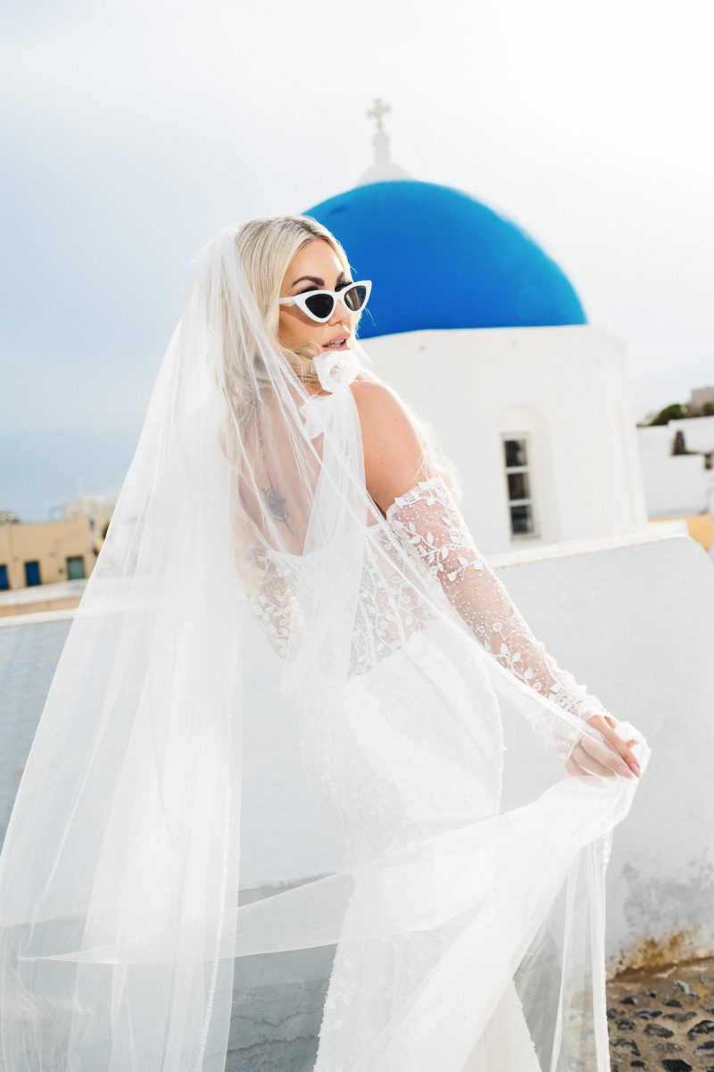 Santorini wedding photographer captures stylish bride with veil near blue dome.