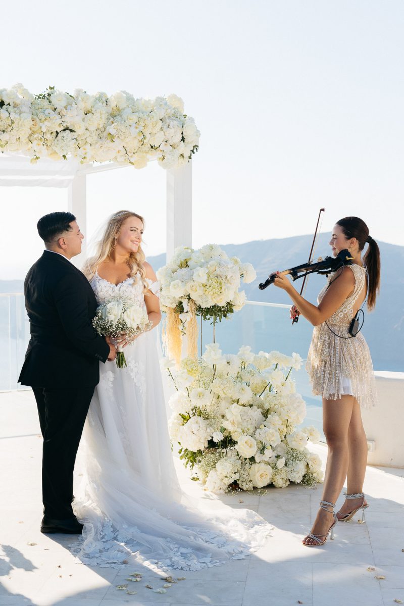 Bride and groom with violinist at ceremony by Santorini wedding photographer